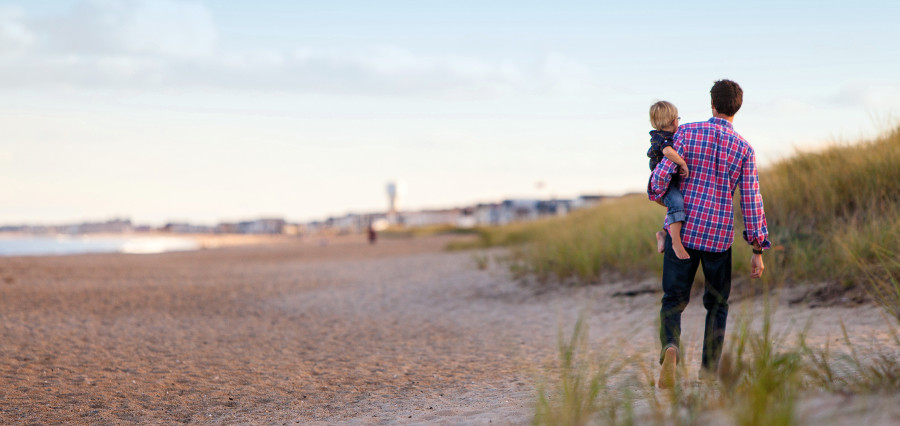 Ein Mann mit einem Kind auf dem Arm an einer Küste.